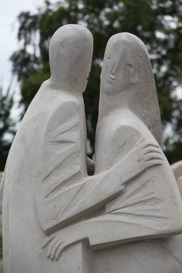 Old ornamental masonry sculpture of man embracing woman near tree in city park